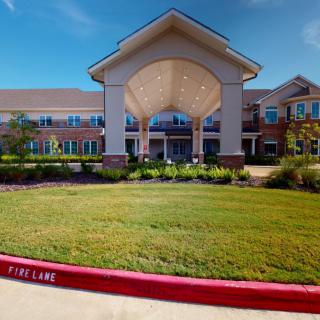 A well-maintained building with a grand entrance and landscaped surroundings under a clear blue sky.
