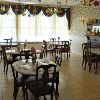 An empty cafe with elegantly decorated tables and chairs, featuring large windows allowing natural light.