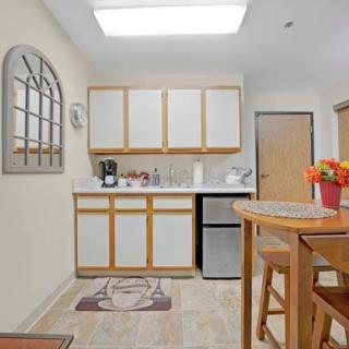 A modern kitchen interior with wooden cabinets, a small refrigerator, and a dining area.
