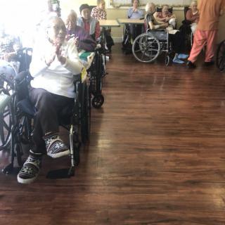 A group of elderly individuals gathered in a nursing home, many in wheelchairs, engaged in a community activity.