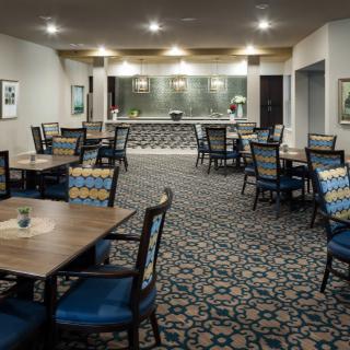 An empty dining area with neatly arranged tables and chairs, featuring a decorative carpet and modern lighting.