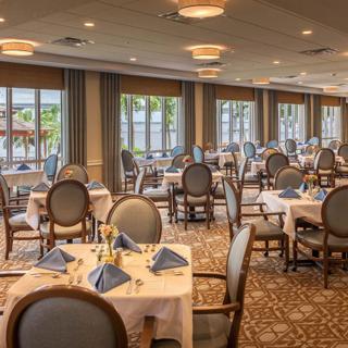An elegant dining room setup with neatly arranged tables and chairs, featuring large windows and decorative napkins.