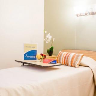 A cozy bedroom setup featuring a neatly made bed with colorful pillows, an orchid plant, and a tray with food.