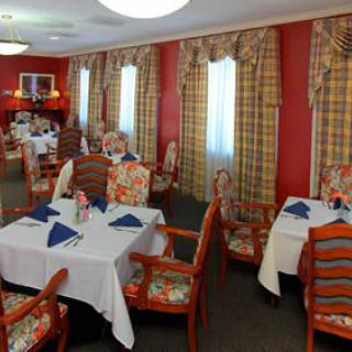 A cozy dining room with neatly arranged tables and chairs, featuring elegant curtains and warm decor.
