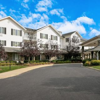 A large residential building with a driveway and landscaped surroundings under a partly cloudy sky.