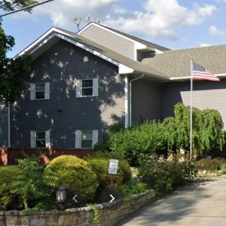 A residential house with a garden and an American flag under a cloudy sky.
