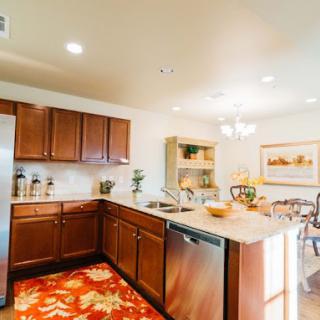 A modern kitchen with wooden cabinets and stainless steel appliances, featuring an open layout leading to the dining area.