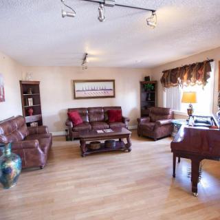 A cozy living room featuring leather sofas, a coffee table, and a piano beside a window with drapes.