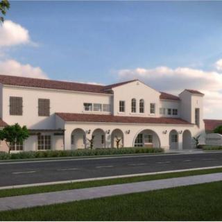 A modern Spanish-style building with arched windows and a tiled roof, surrounded by a landscaped area.