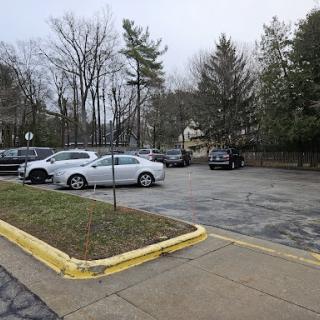 A view of an empty parking lot with several parked cars surrounded by trees on a cloudy day.