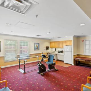 A therapy room with exercise equipment and a small kitchen area, featuring a carpeted floor.