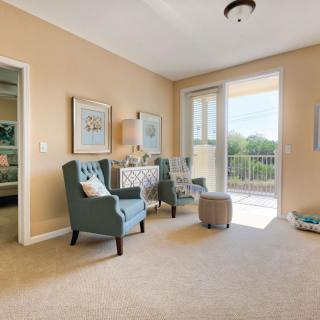A bright living room with comfortable chairs, a small side table, and access to a balcony.