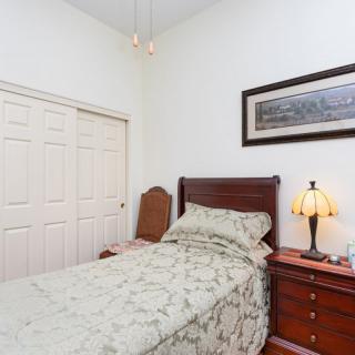 A neatly arranged bedroom with a single bed and wooden furniture, featuring a cozy lamp and artwork on the wall.