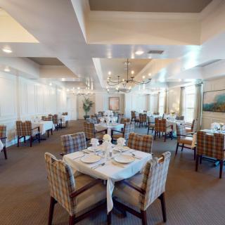 An elegant restaurant dining room with neatly arranged tables and chairs, adorned with chandeliers and wall artwork.