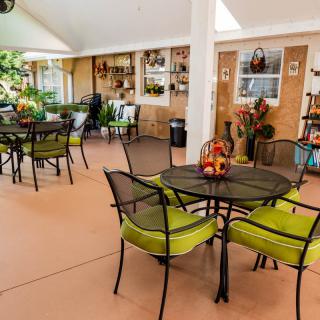 A beautifully decorated patio with tables and green-cushioned chairs, surrounded by plants.