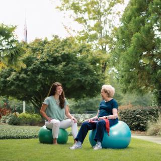 Two people sitting on exercise balls having a conversation in a park.