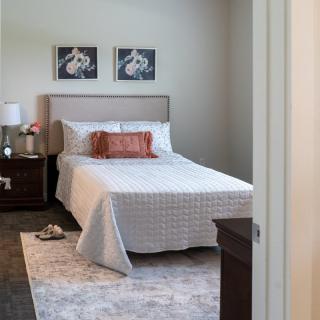 A neatly arranged bedroom featuring a bed with white bedding, decorative pillows, nightstand, and wall art.