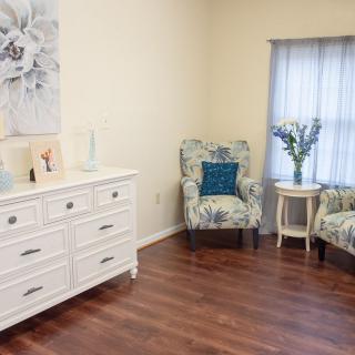 A cozy living room with elegant decor, featuring floral armchairs, a white dresser, and wooden flooring.