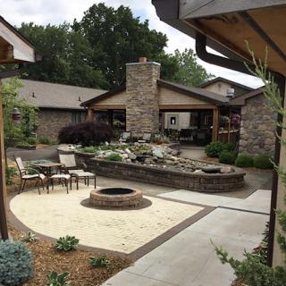 A serene outdoor space featuring a landscaped patio, fire pit, and water feature surrounded by lush greenery.