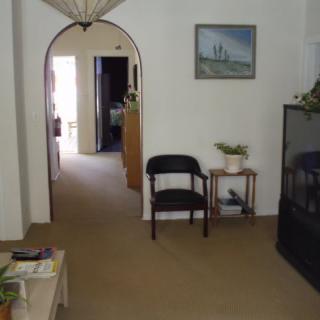 A cozy living room with an archway, featuring a chair, side table with a plant, and a television.