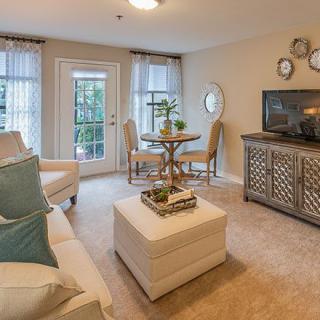 A cozy living room featuring a sofa, armchairs, and a TV stand, with natural light streaming through the windows.