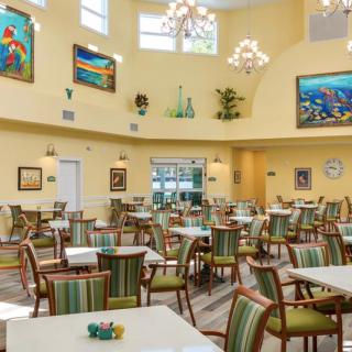 A spacious dining room featuring multiple tables and chairs, with colorful paintings decorating the walls.