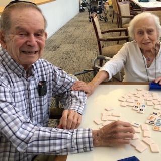 Two elderly individuals playing a game at a table, smiling and enjoying their time together.