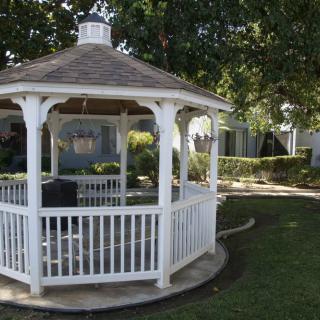 A white gazebo surrounded by a well-maintained garden with lush green grass and trees.