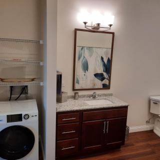 A combined bathroom and laundry area featuring a vanity with a mirror, a washer/dryer unit, and wall artwork.