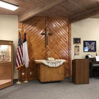 A church interior featuring a wooden altar with a cross, flanked by American and Christian flags, alongside a pulpit.