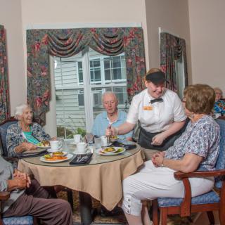 A group of seniors enjoying a meal together at a restaurant, served by a waiter.