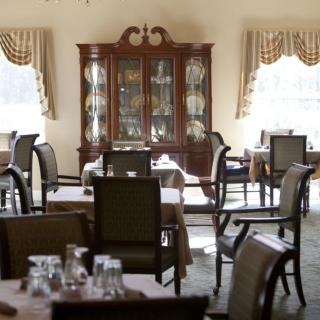 A formal dining room with neatly arranged tables and chairs, featuring a china cabinet and elegant curtains.