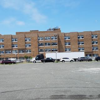 A brick building with multiple windows and parked vehicles in the foreground.