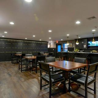 A modern restaurant interior featuring wooden tables and chairs with a bar area in the background.