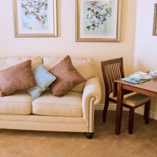 A cozy living room with a beige sofa adorned with cushions, complemented by wall art and a small dining area.