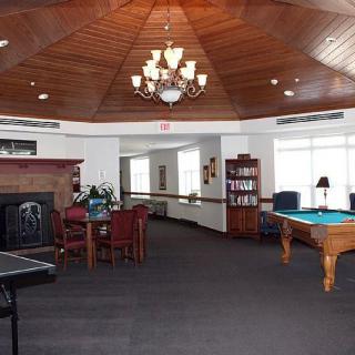 A spacious recreation room featuring a pool table, chess table, ping pong table, and bookshelf under a wooden ceiling with a chandelier.