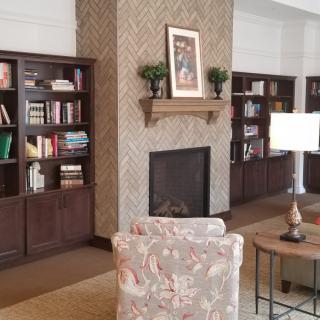 A cozy living room with a fireplace surrounded by bookshelves, an armchair, and a lamp.