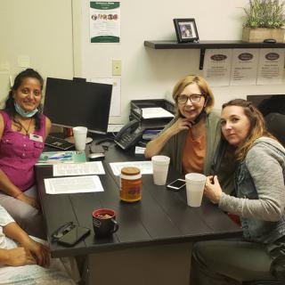 A group of people gathered around a desk for a meeting in an office setting.