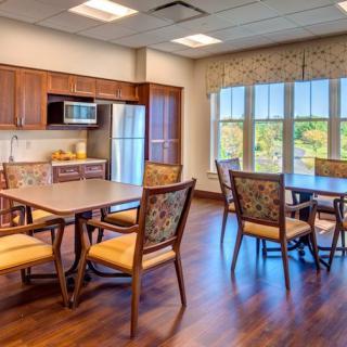 A cozy kitchen and dining area with wooden floors, featuring a fridge, microwave, and tables with chairs by the window.