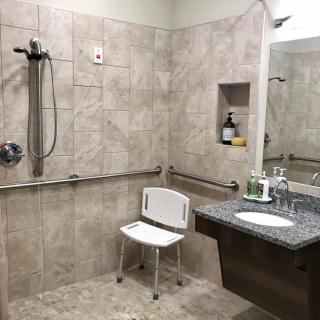 A modern accessible bathroom with a shower chair and grab bars for safety.