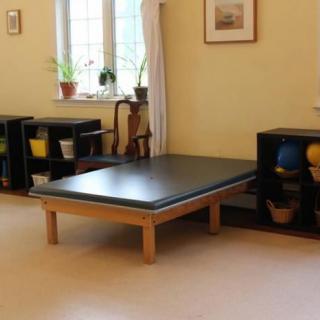 A therapy room equipped with a large exercise mat and storage for rehabilitation equipment.