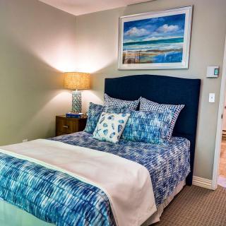 A cozy bedroom with a blue-themed bedding set, a bedside lamp, and artwork above the bed.