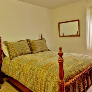A cozy bedroom with a traditional wooden bed and patterned bedding, featuring a mirror on the wall.