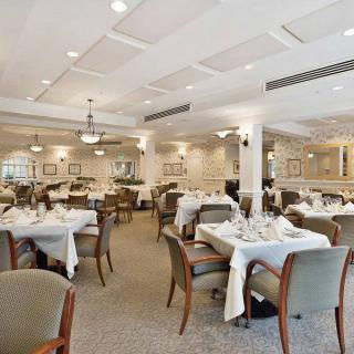 An elegant dining room with neatly arranged tables and chairs, featuring white tablecloths and warm lighting.