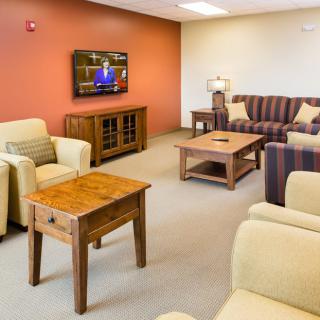 A cozy living room with comfortable sofas, chairs, and a television on the wall.