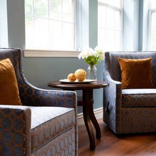 A cozy living room corner with two armchairs, a small round table, and a bright window.