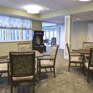 A cozy dining area with several tables and chairs, well-lit by overhead lighting and natural light from the windows.