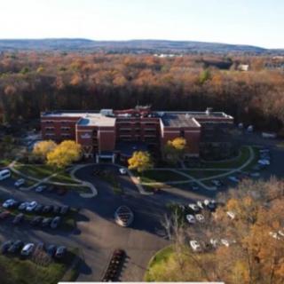 Aerial view of a brick building surrounded by autumn foliage and a parking lot.
