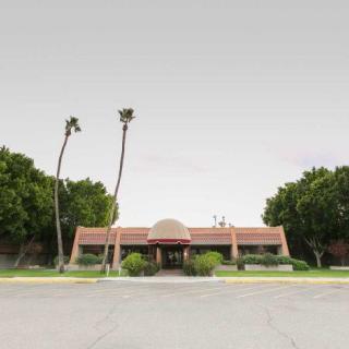 A single-story building with a red-tiled roof and an entrance surrounded by palm trees against an overcast sky.