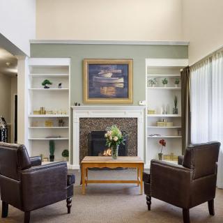 A cozy living room featuring two leather chairs facing a fireplace, with decorative shelves and a painting above the mantel.